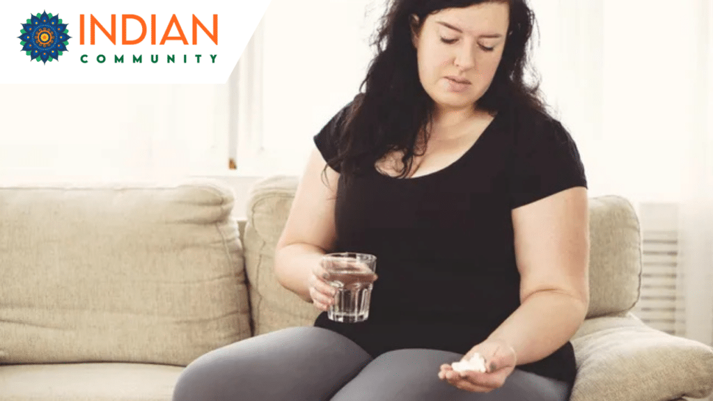 A woman sitting, holding a handful of medicines in one hand and a glass of water in the other.