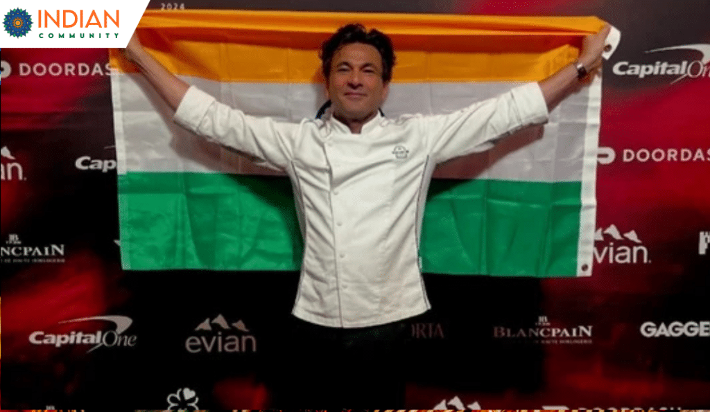 Chef Vikas Khanna, dressed in a white chef's coat, proudly holds up the Indian flag behind him with a big smile