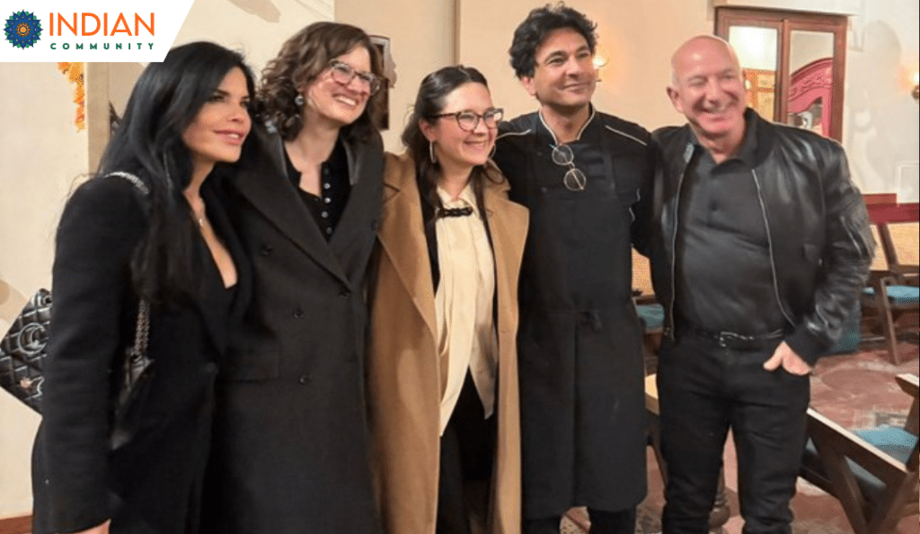 A group of five people, including Jeff Bezos, Lauren Sanchez and chef Vikas Khanna, pose for a photo inside a warmly lit venue.