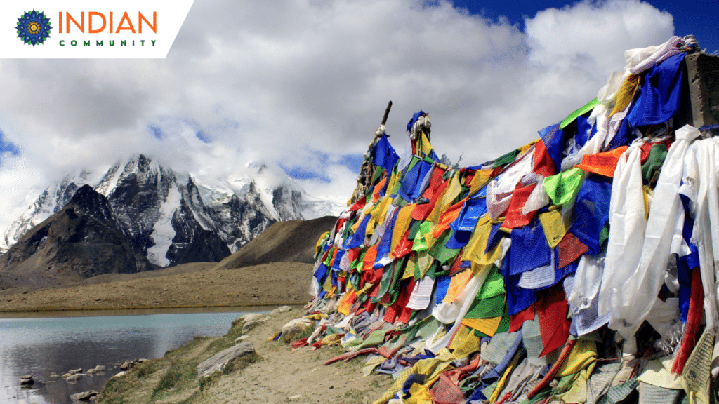 A breathtaking landscape featuring snow-capped mountains under a partly cloudy sky, with colorful prayer flags fluttering in the foreground.