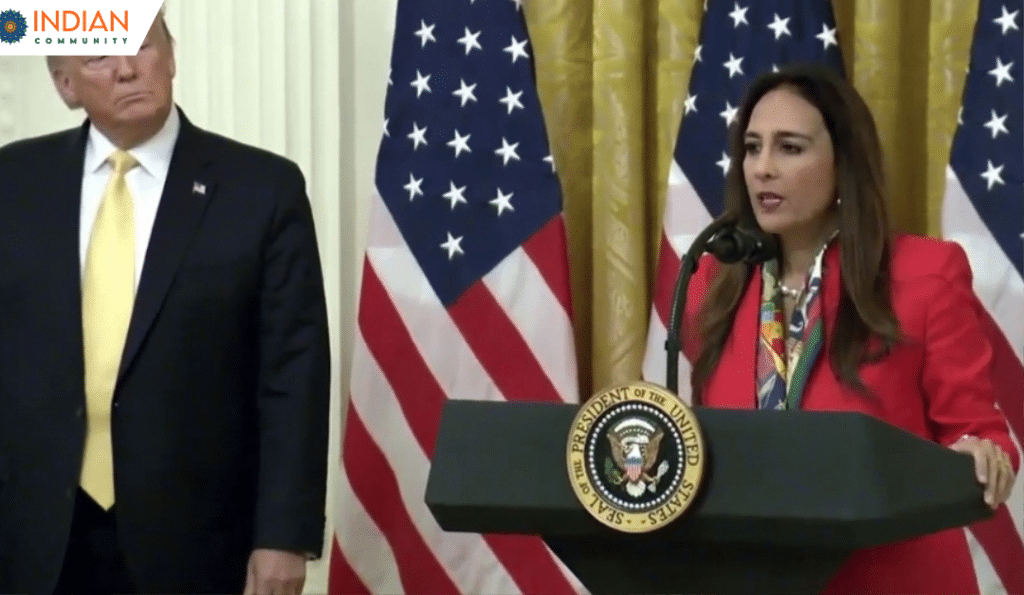 Harmeet Dhillon in a red blazer speaks at a podium with the Seal of the President of the United States and Trump is standing besides her.