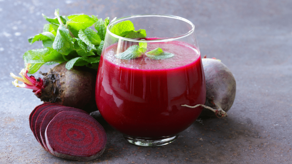 A vibrant, refreshing glass of Beetroot Kanji, served with sliced beetroot and carrot, showcasing its deep pink color and healthful properties.