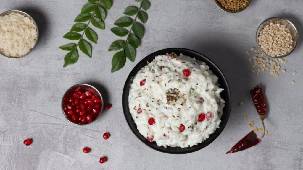 A bowl of creamy curd rice garnished with pomegranate seeds and coriander leaves.