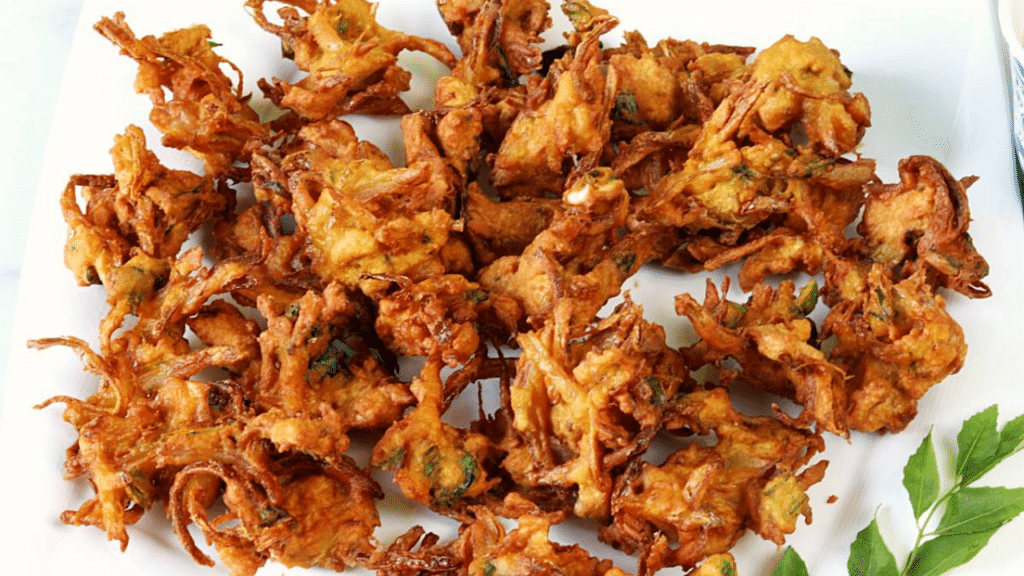 Crispy vegetable pakoras served with mint chutney on a plate.