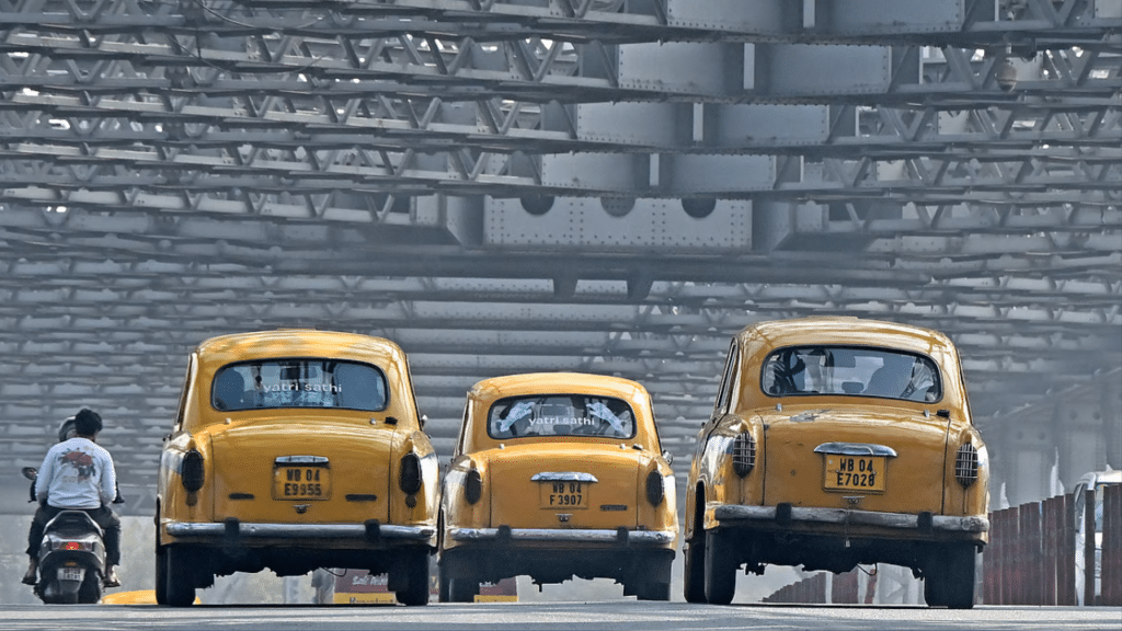 Passengers riding Hindustan Ambassador yellow taxis along the Howrah bridge in Kolkata