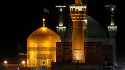Illuminated mosque at night with a golden dome and minarets against a dark sky.