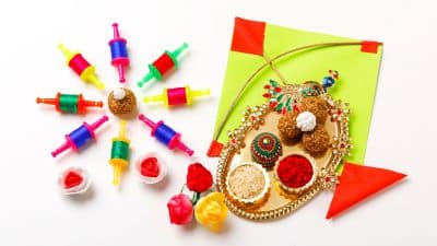 Colorful Holi festival items including kite strings, roli, chawal, sweets, and decorative trays arranged on a white background.